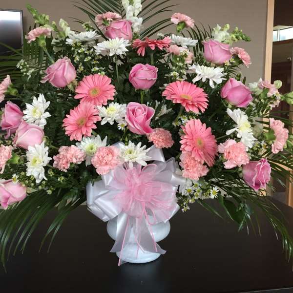 Pink and white floral arrangement in a white vase with a pink bow