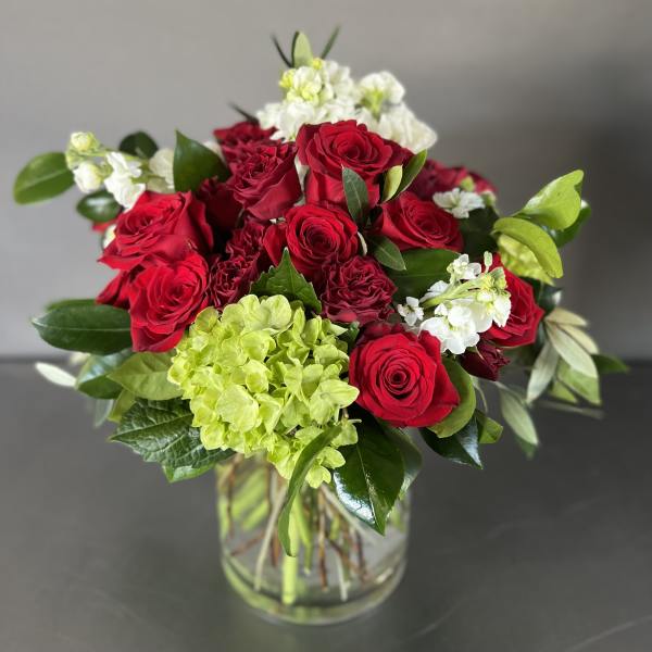 Bouquet of red roses, white flowers, and green hydrangea in a glass vase