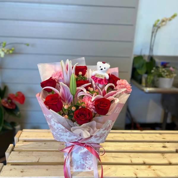 Bouquet of red roses and pink lilies with a small teddy bear