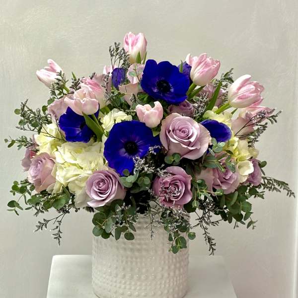 Pink tulips, lavender roses, and blue anemones in a white vase