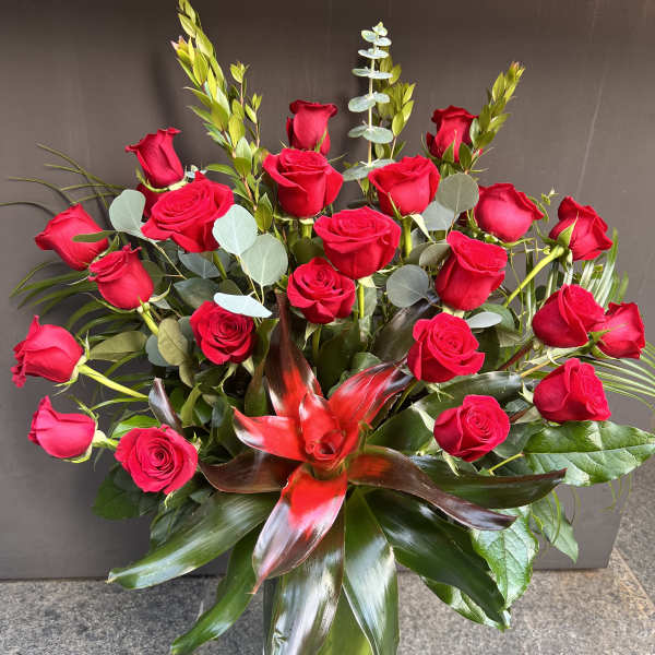 Red roses arranged in a clear glass vase with tropical foliage