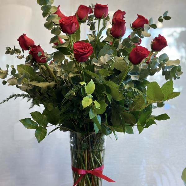 Tall bouquet of red roses in a clear glass vase with a red ribbon