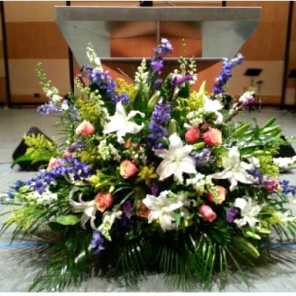 Large altar arrangement with white lilies, peach roses, and purple flowers on a stage
