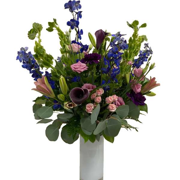 Tall mixed bouquet with blue flowers, pink roses, and dark calla lilies in a glass vase