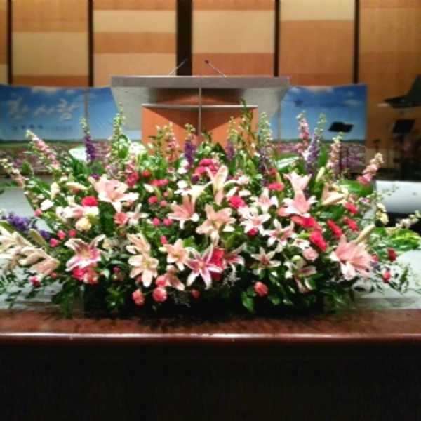 Large stage arrangement of pink lilies and red flowers in front of a podium