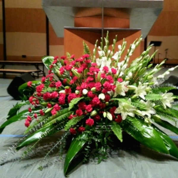 Large red carnation and white lily stage arrangement with abundant foliage in front of a podium