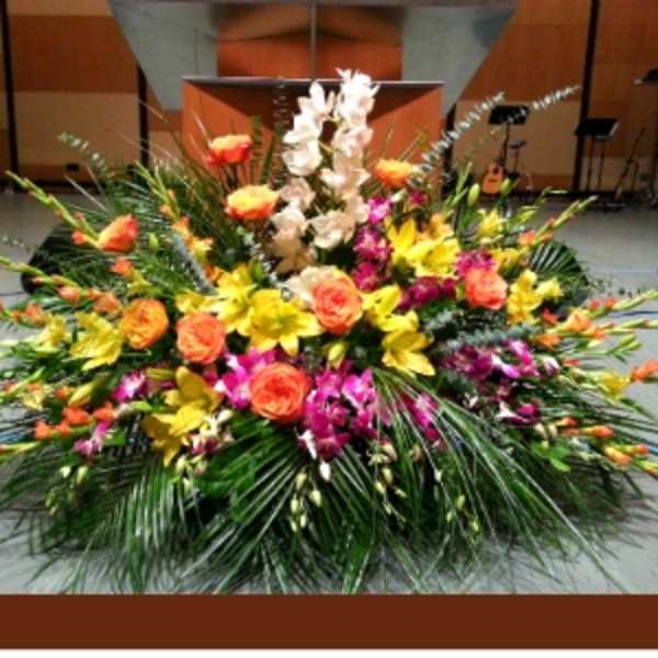 Large stage arrangement with yellow lilies, orange roses, and pink orchids in a fan-shaped design