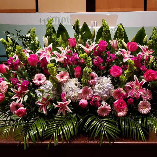 Large pink and white floral stage arrangement with lilies, roses, gerbera daisies, and hydrangeas