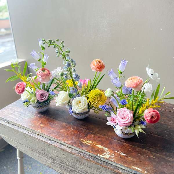 Three small pastel flower arrangements in patterned bowls on a rustic wooden table