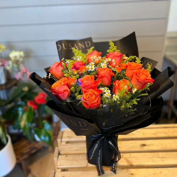 Bouquet of orange roses with small white filler flowers in black wrap