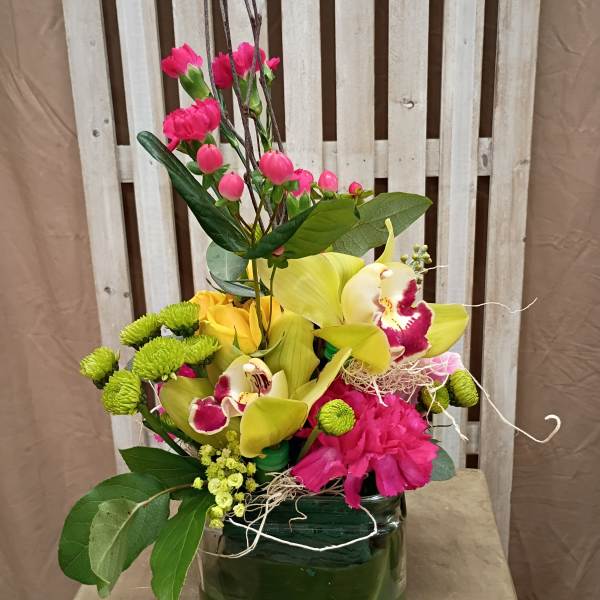 Mixed floral arrangement in a green glass vase with yellow orchids and pink blooms