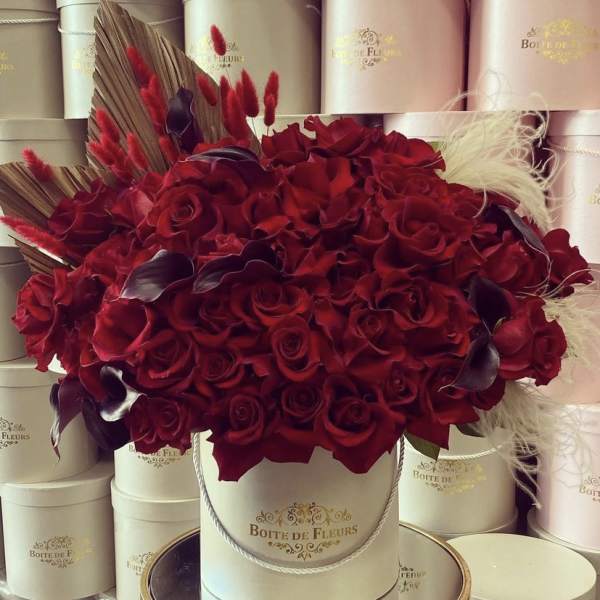 Red rose arrangement in a round hat box with decorative feathers