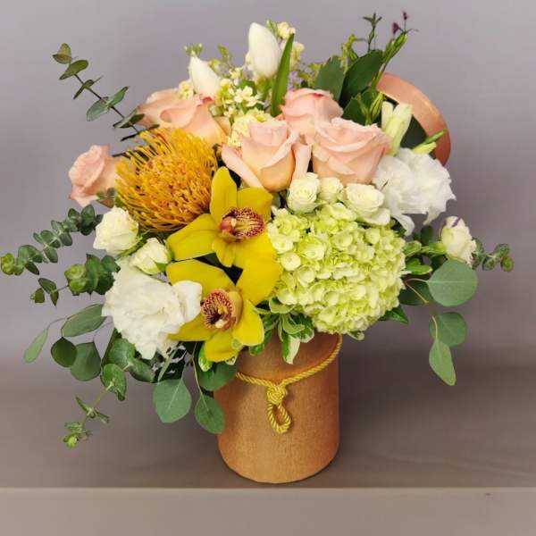 Bouquet of pale pink roses, yellow orchids, and white blooms in a gold vase