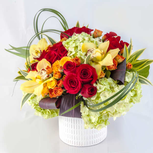 Bouquet of red roses, yellow orchids, and green hydrangeas in a white vase
