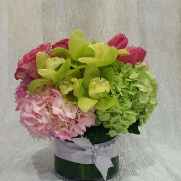 Pink hydrangeas and green orchids in a round vase with a ribbon