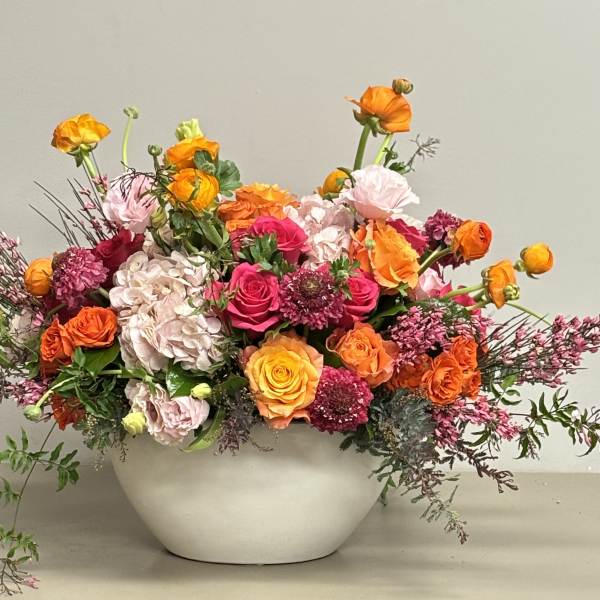 Low centerpiece of bright orange and pink flowers with pale hydrangea in a round white bowl