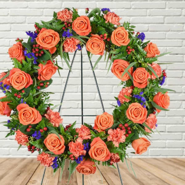 Circular floral wreath with orange roses and pink carnations on a stand