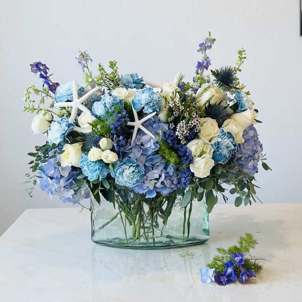 Blue and white floral arrangement in a glass vase with starfish accents