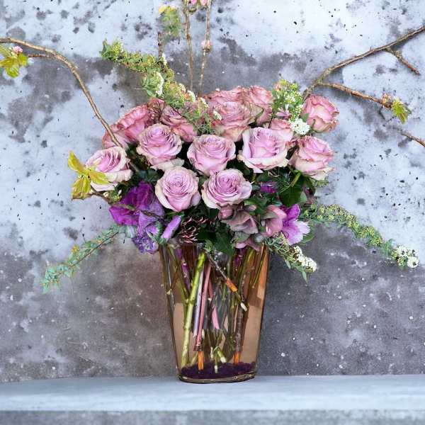 Pink roses and purple flowers arranged in a tall glass vase