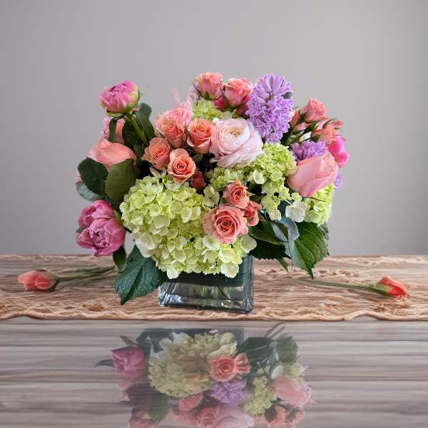 Pink and lavender flowers arranged in a square glass vase