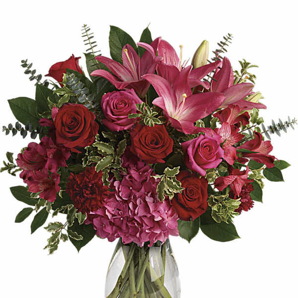 Bouquet of pink lilies, red roses, and hydrangeas in a clear glass vase