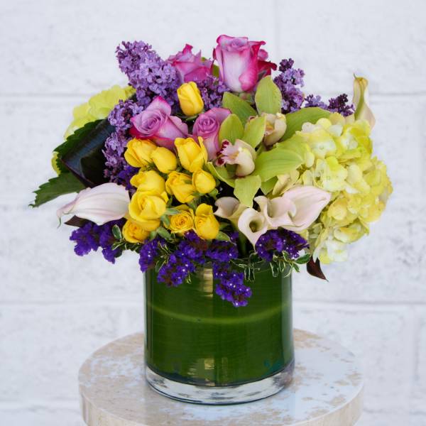 Mixed bouquet of roses, orchids, and hydrangeas in a green glass vase
