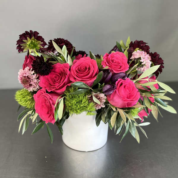 Pink roses and dark burgundy flowers arranged in a white vase