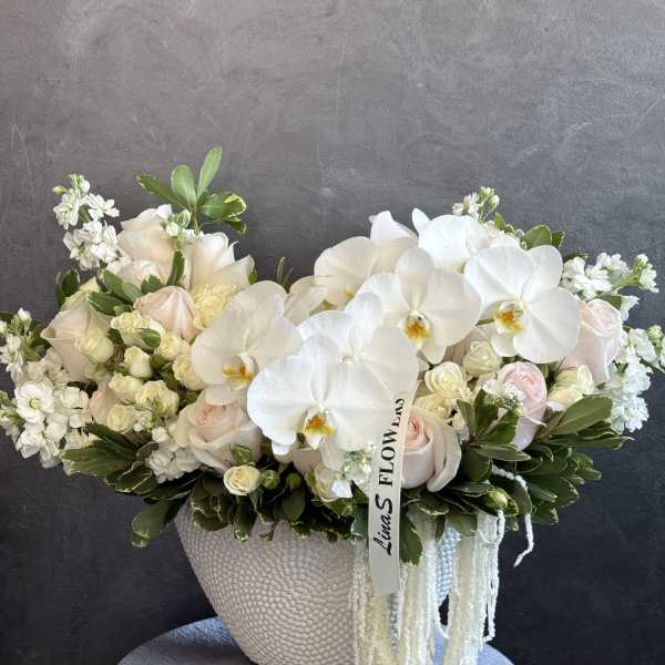 White orchids and pale roses in a textured vase with trailing white strands