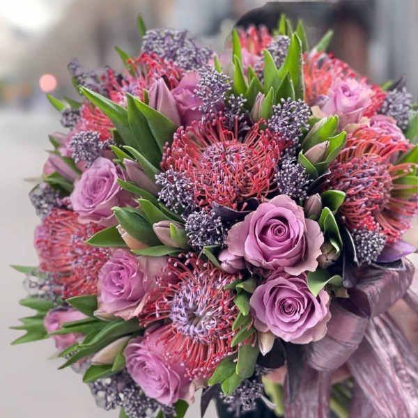 Lavender roses and pink pincushion protea bouquet with green foliage