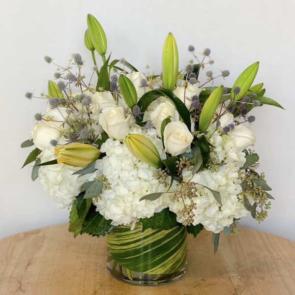 White roses and lilies arranged in a glass vase with hydrangeas