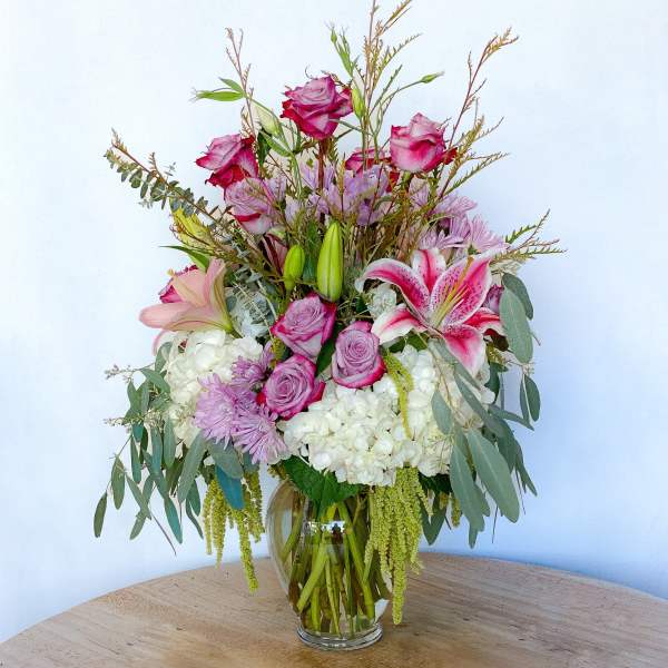 Bouquet of pink roses, lilies, and lavender flowers in a glass vase