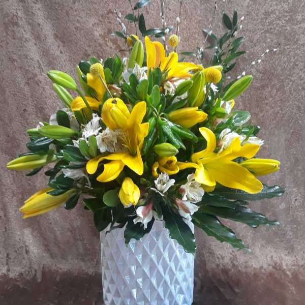 Yellow lilies and white flowers arranged in a white textured vase