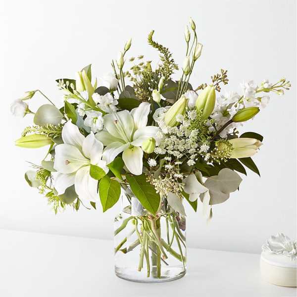 White lilies and mixed white flowers in a clear glass vase