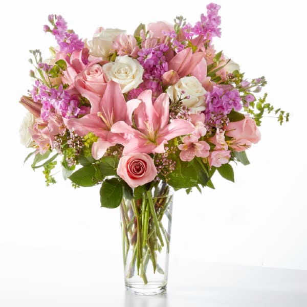 Tall clear glass vase of pink lilies, roses, white roses, and lavender blooms.