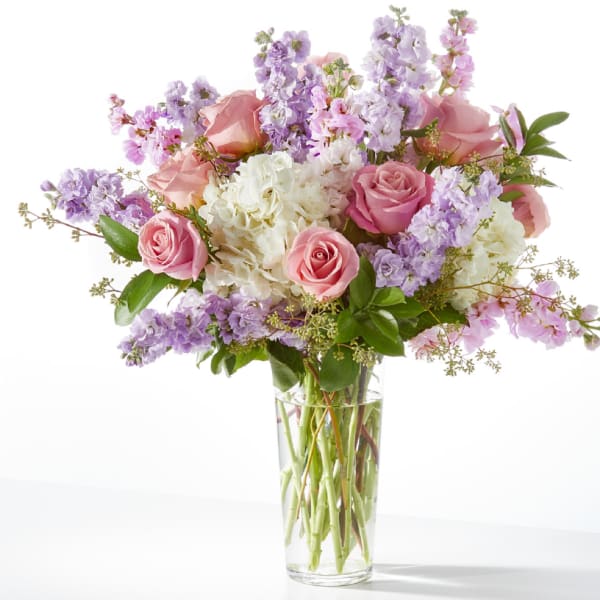 Tall glass vase of pink roses, white hydrangeas, and lavender stock flowers