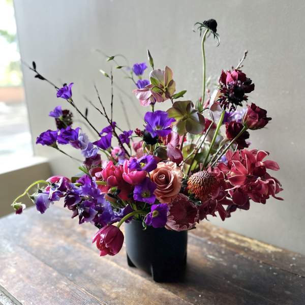 Mixed bouquet of purple, pink, and burgundy flowers in a black vase