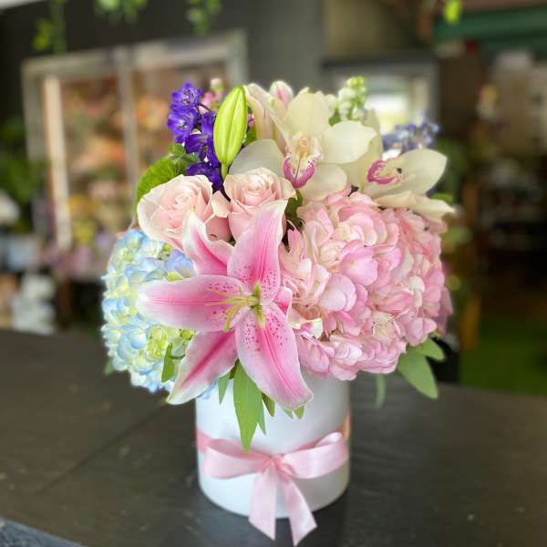 Pink and white floral arrangement in a white hatbox with a pink ribbon