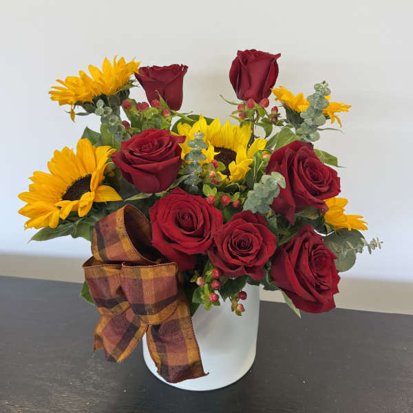Arrangement of red roses and yellow sunflowers in a white container with a plaid bow.