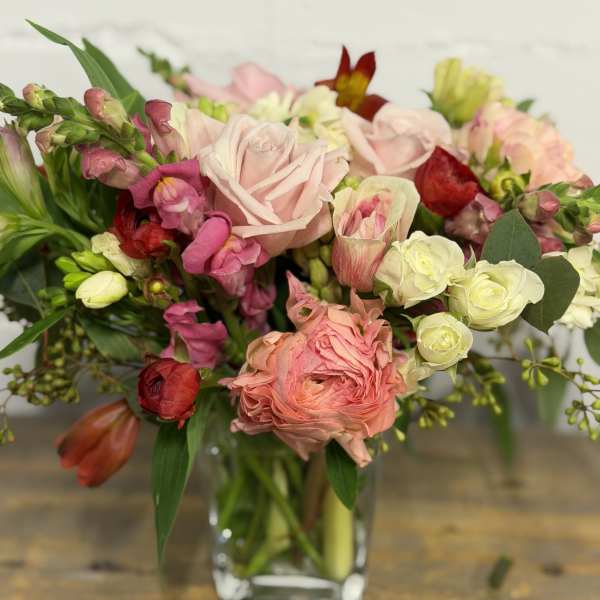Mixed bouquet of pink, peach, and white flowers in a clear glass vase