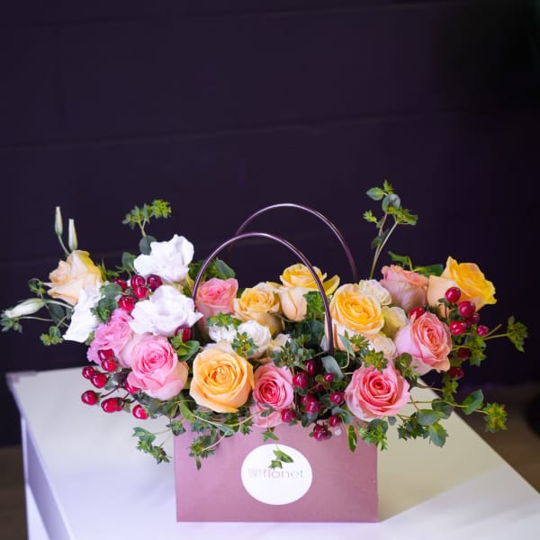 Pink and yellow roses arranged in a mauve gift bag