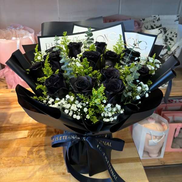 Bouquet of black roses with white filler flowers wrapped in glossy black paper and ribbon