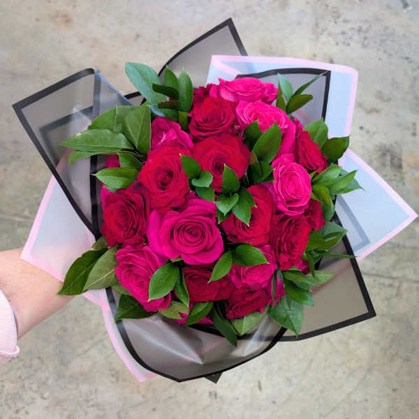 Handheld bouquet of bright pink roses with green foliage in pastel and black wrap