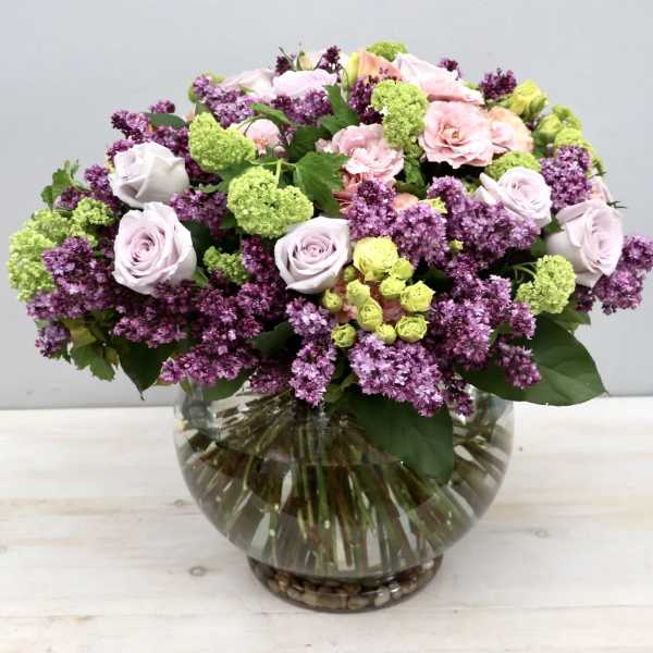 Mixed bouquet of pink and lavender flowers in a round glass vase