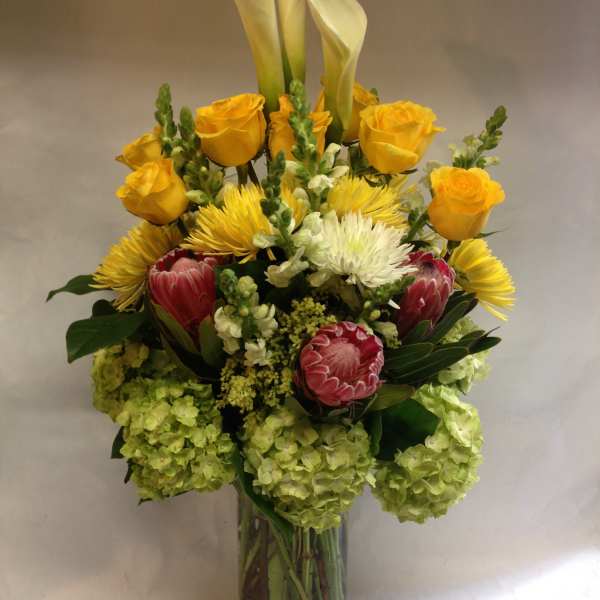 Mixed bouquet with yellow roses, white calla lilies, and pink protea in a glass vase