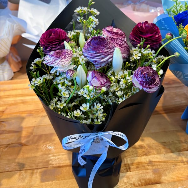 Bouquet of purple ranunculus and white accent flowers wrapped in black paper