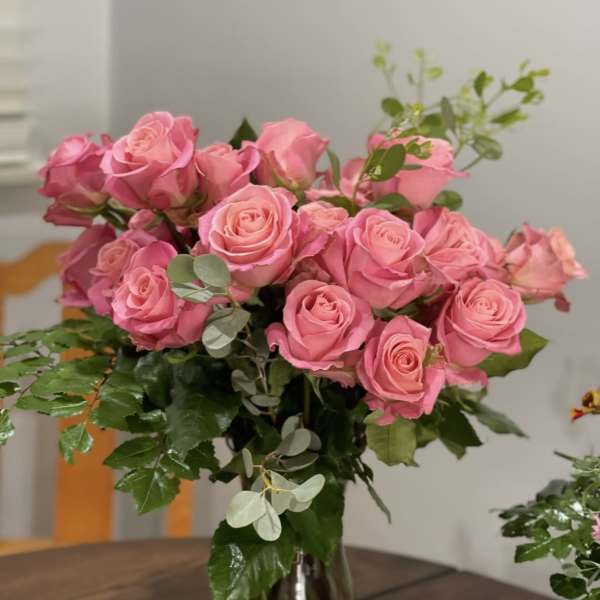 Pink roses arranged in a clear glass vase with greenery