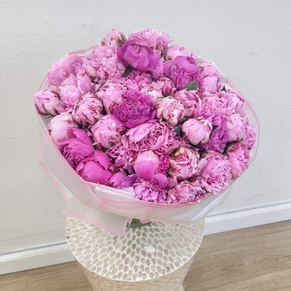 Large pink bouquet of peonies wrapped in translucent paper
