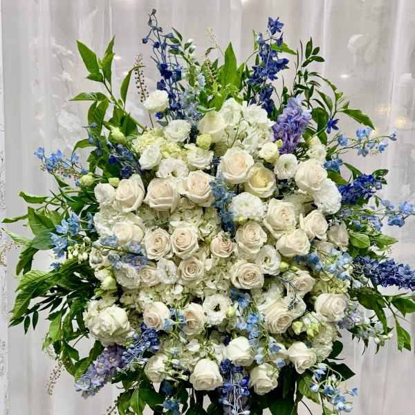Large standing floral spray with white roses and blue flowers on an easel