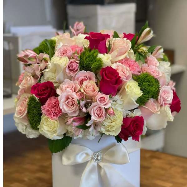 Round hatbox arrangement of pink and white roses with hot pink accents and green dianthus in a white box with satin bow