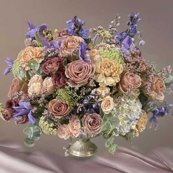 Large pastel bouquet of roses, carnations, and blue flowers in a silver vase